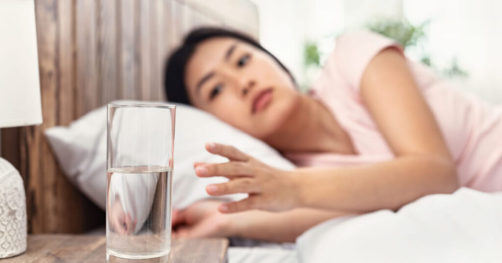 Woman lying in bed and reaching for a glass of waters