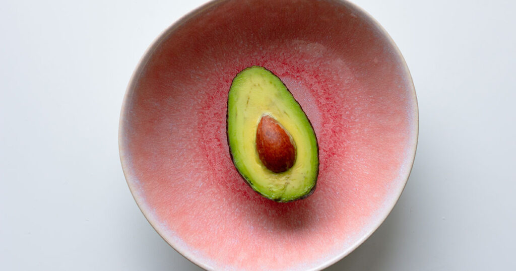 Fresh avocado in the pink bowl on the table. Healthy avocado fats.
