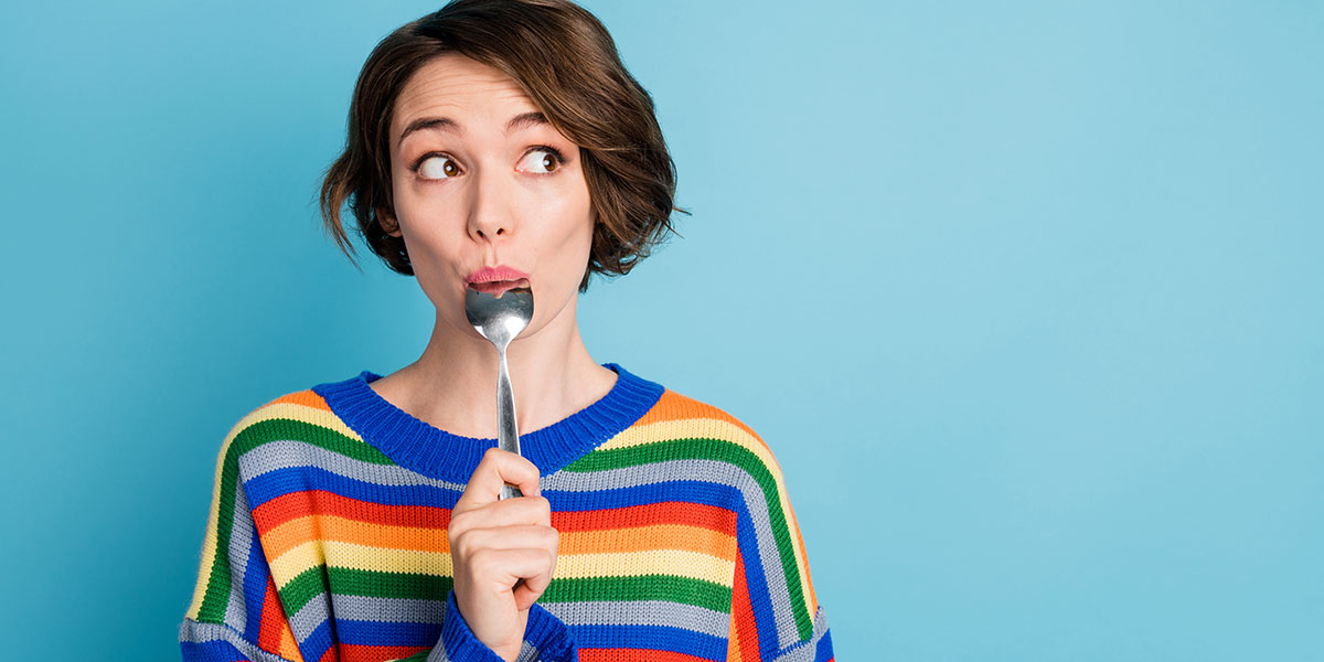 A woman in a colourful sweater eats food with a spoon.